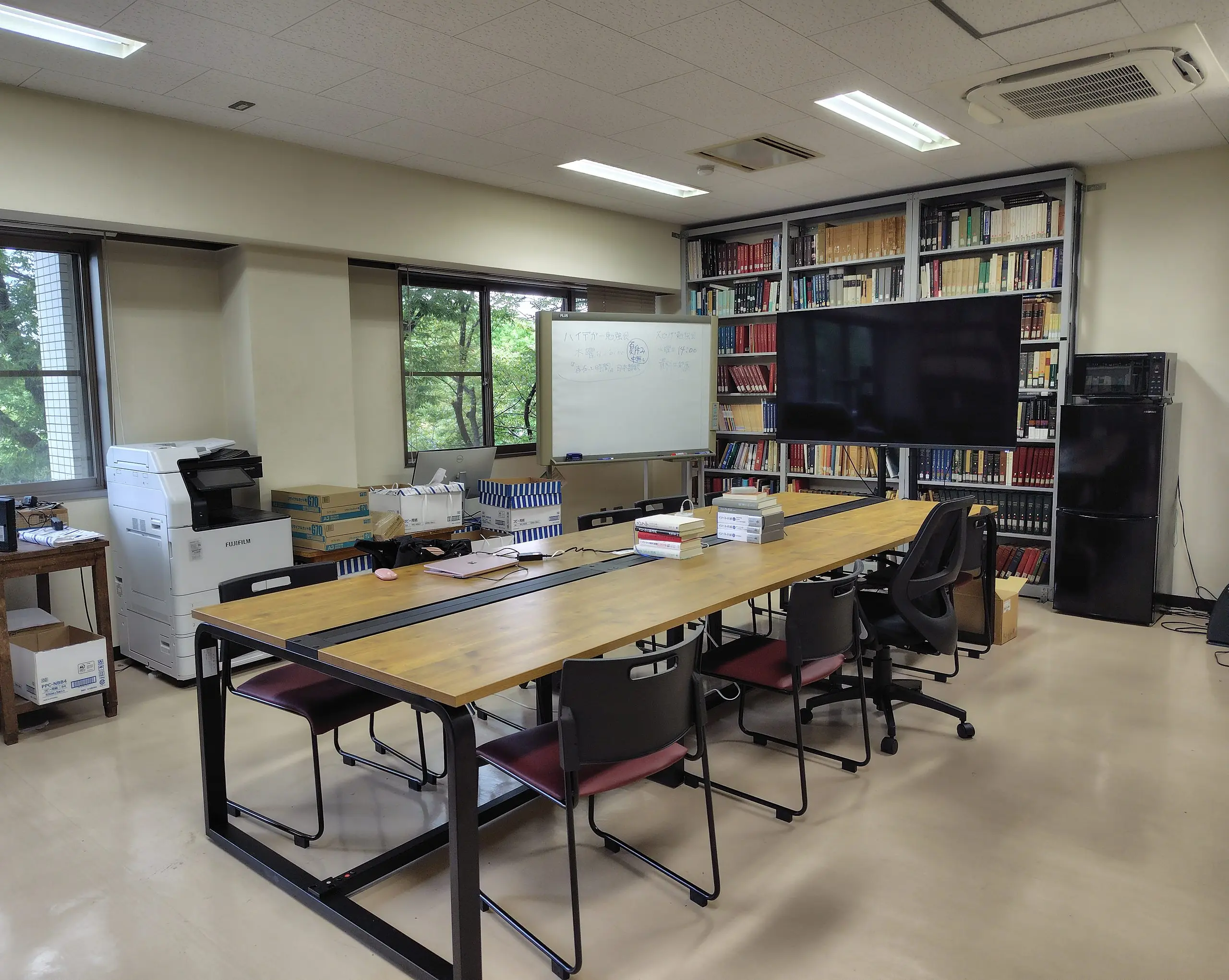哲学リテラチャーラボ（311号室）の全景。長机とホワイトボード、大型モニタ、本棚